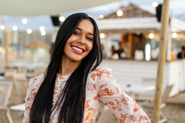 Photo belle et souriante femme brésilienne regardant le concept de vacances de luxe de la caméra dans la station balnéaire au coucher du soleil xa