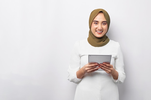 Belle souriante sympathique jeune femme musulmane asiatique arabe portant le hijab vert tenant une tablette numérique tout en regardant la caméra isolée sur fond blanc Concept de style de vie religieux de personnes