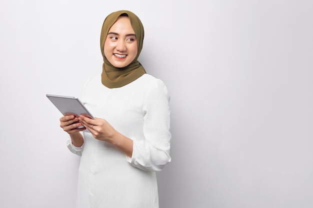 Belle souriante sympathique jeune femme musulmane asiatique arabe portant le hijab vert tenant une tablette numérique tout en regardant un espace vide isolé sur fond blanc Concept de style de vie religieux de personnes