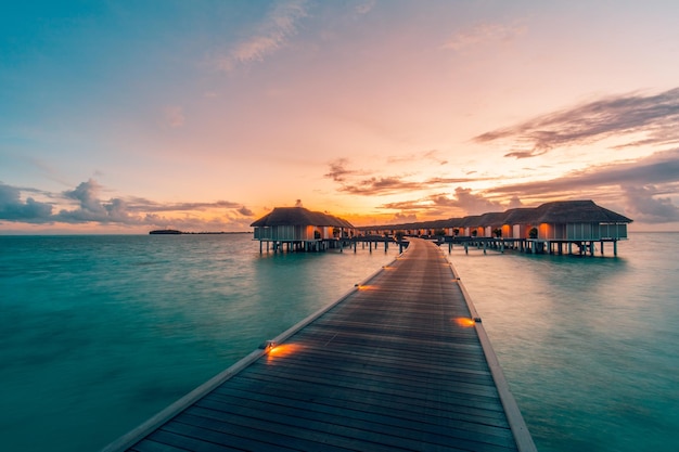 Belle station balnéaire tropicale de luxe, villas sur l'eau avec des lumières sous le ciel du coucher du soleil. Jetée sur la baie du lagon