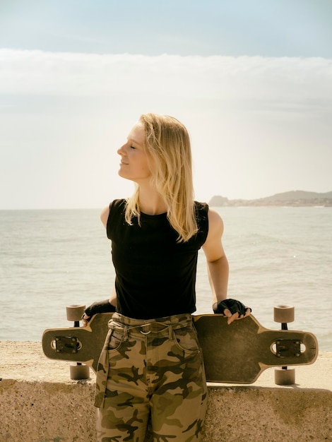 Belle et style jeune fille posant avec une planche à roulettes au bord de mer. Fille jouissant de la liberté.