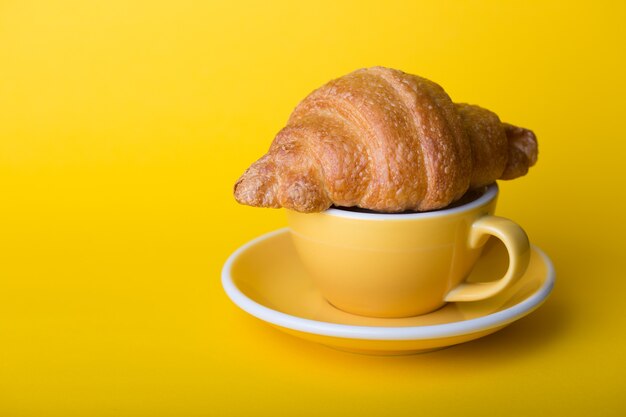 Belle tasse de café jaune cappuccino avec croissant sur fond jaune