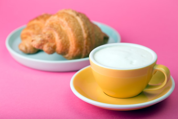 Belle tasse de café jaune avec cappuccino et croissant sur fond rose