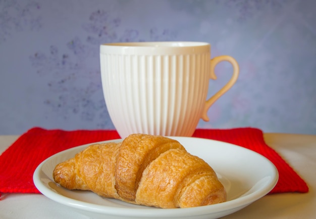 Belle tasse de thé blanc avec un croissant sur une écharpe tricotée rouge