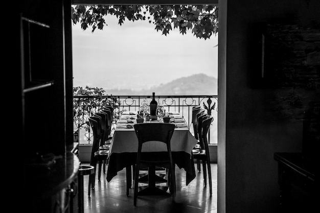 Belle terrasse d'un restaurant. Prêt pour l'arrivée des invités. Table servie. Verres, assiettes et vin. Noir et blanc