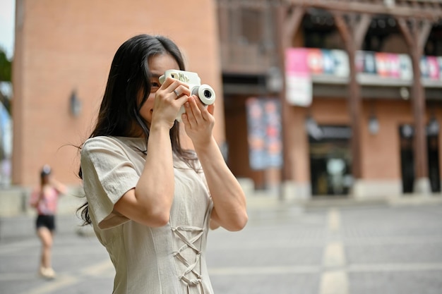 Une belle touriste asiatique se promenant dans des paysages urbains avec son appareil photo instantané