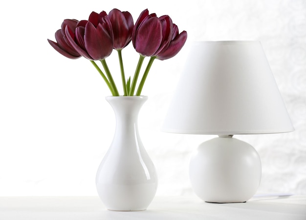 Belle tulipe violette dans un vase avec lampe sur fond clair