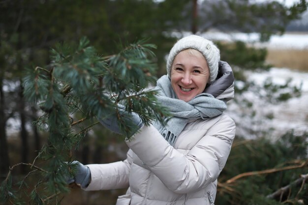 Belle vieille femme âgée à la retraite heureuse adulte âgée à la retraite avec un arbre de Noël dans la forêt d'hiver s'amuser et sourire et profiter de la neige prend l'arbre de Noël à la maison de la forêt