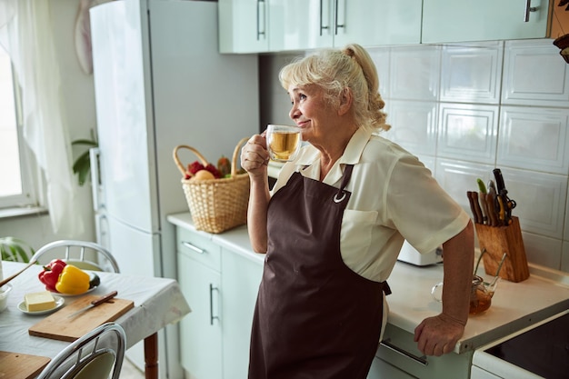 Belle vieille femme buvant une tisane dans la cuisine