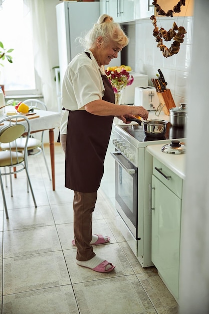 Belle vieille femme en tablier préparant le dîner à la maison