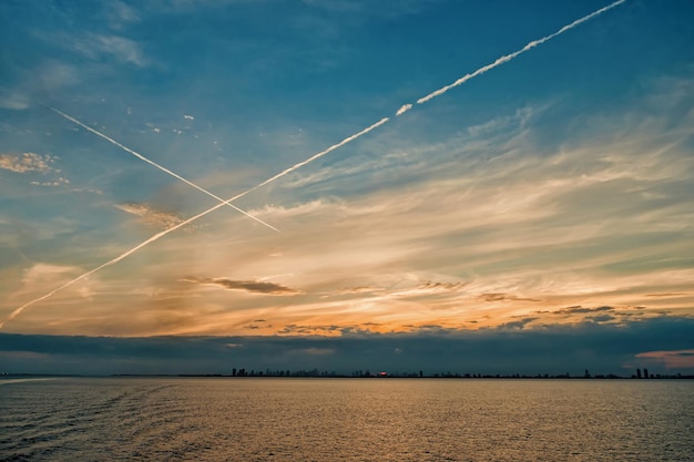 Belle ville au lever ou au coucher du soleil ciel bleu avec nuages et lignes d'avion, maisons à l'horizon avec mer, eau de mer en plein air comme fond de paysage naturel