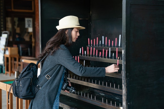 belle visiteuse asiatique faisant un vœu de santé et de fortune puis offrant une bougie sur l'autel de la bougie dans le sanctuaire japonais.