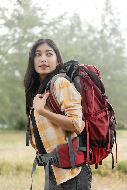 Belle voyageuse asiatique backpacker portant un gros sac rouge dans la forêt à la recherche de côté.