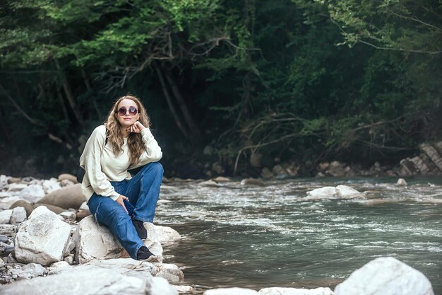 Belle voyageuse aux longs cheveux ondulés sur fond de forêt verte et de rivière de montagne