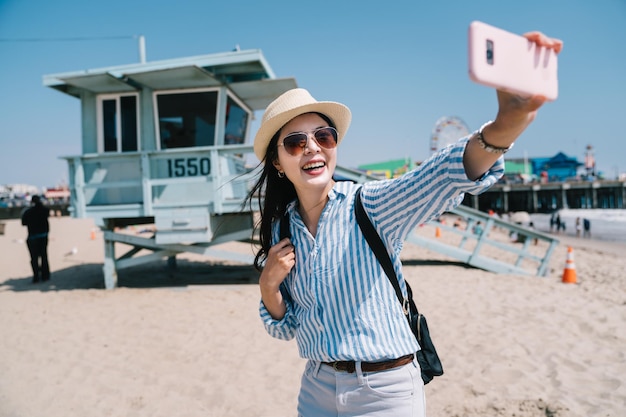 une belle voyageuse prenant un selfie avec le poste de secours près de son smartphone rose