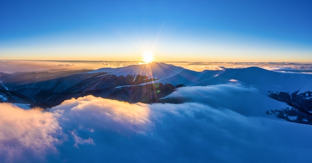 Belle vue envoûtante sur les montagnes et les rochers avec forêt d'épicéas par une soirée d'hiver glaciale avec brouillard et soleil couchant. Concept de nature hivernale rude