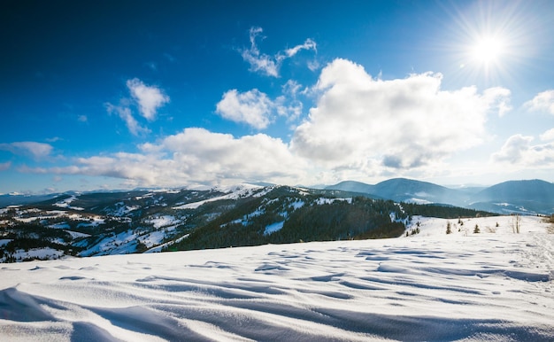 Belle vue envoûtante sur les pentes des montagnes avec des bosquets denses d'arbres et des congères contre le ciel et des nuages blancs par une froide journée d'hiver. Concept de station de ski et détente à la montagne