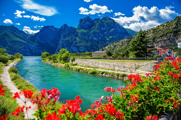 Belle vue d'été sur la rivière Sarca à travers des fleurs rouges dans une petite ville Torbole, lac de Garde, Italie