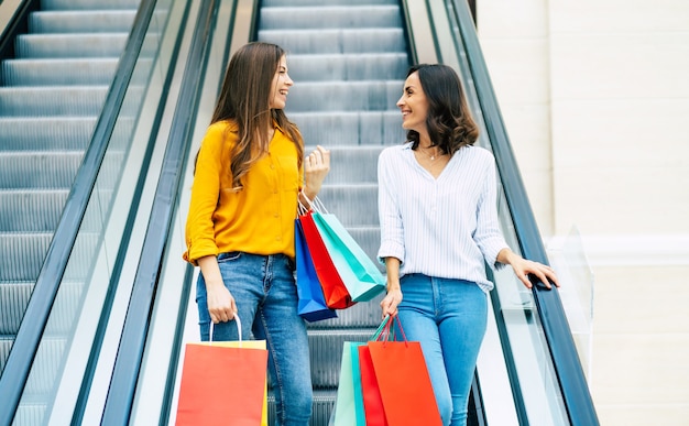 Belles amies de jeune fille heureuse et excitée avec des sacs en papier se promènent dans le centre commercial