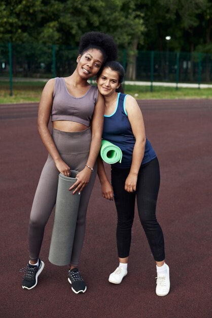 De belles amies se tiennent avec des tapis de sport dans la rue et se préparent pour le sport