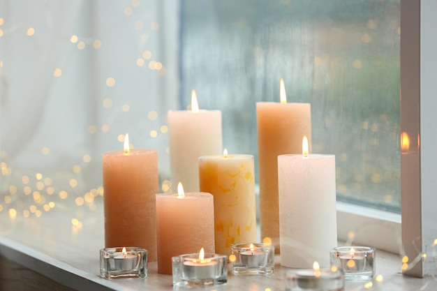 Belles bougies allumées et guirlandes lumineuses au rebord de la fenêtre le jour de la pluie