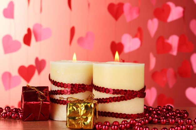 Belles bougies au décor romantique sur une table en bois sur fond rouge