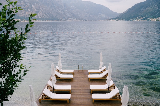 Belles chaises longues blanches et parasols sur la jetée de la baie de Kotor, Monténégro