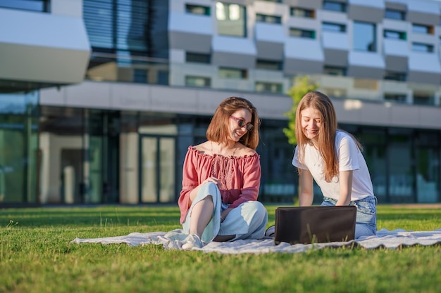 De belles étudiantes s'assoient sur l'herbe verte regardent dans un ordinateur