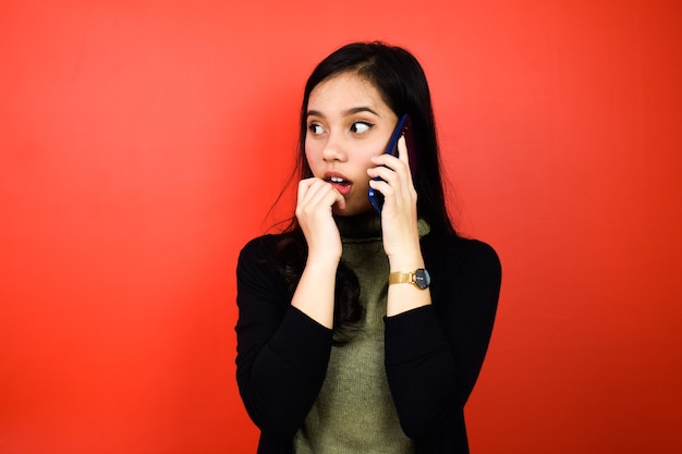 Belles femmes asiatiques utilisant un pull noir choquant et parlant au téléphone portable isolé sur rouge