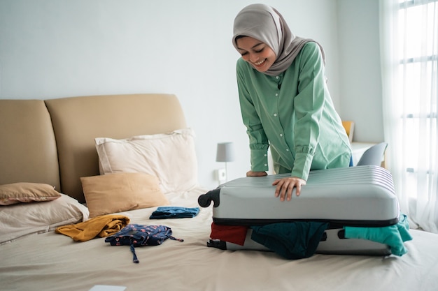 Belles femmes musulmanes essayant de fermer sa valise pleine