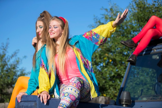 De belles filles de la campagne habillées dans le style des années 90 s'assoient sur un tracteur