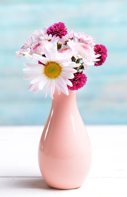 Belles fleurs dans un vase sur table sur fond bleu clair