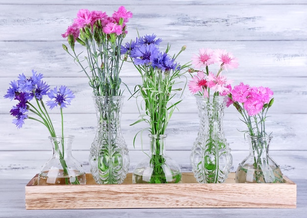 Belles fleurs d'été dans des vases sur fond de bois gris