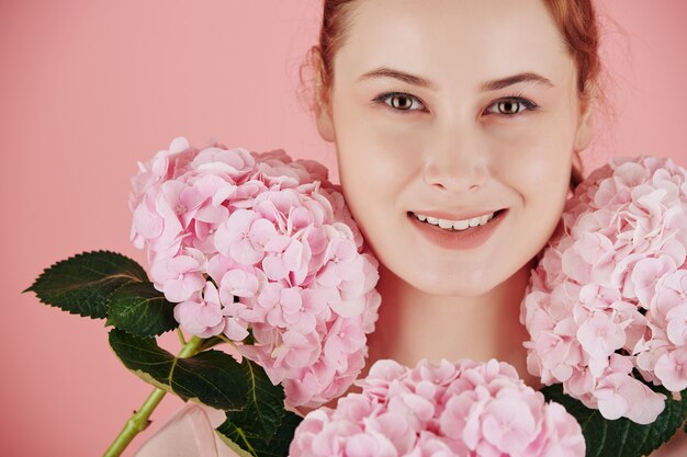 Belles fleurs d'hortensia rose en fleurs autour du visage d'une jolie jeune femme souriante
