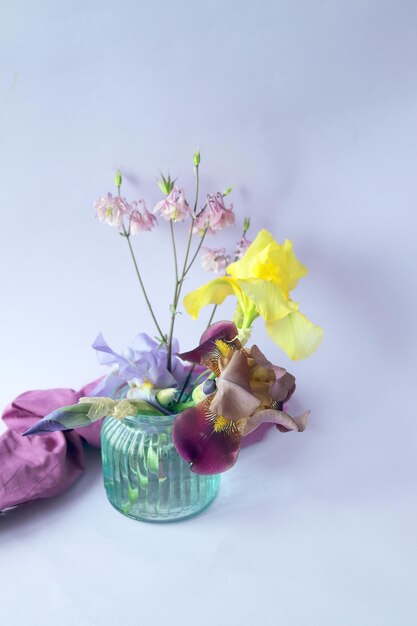 De belles fleurs d'iris jaunes et violettes dans des vases en verre sur un fond lilas