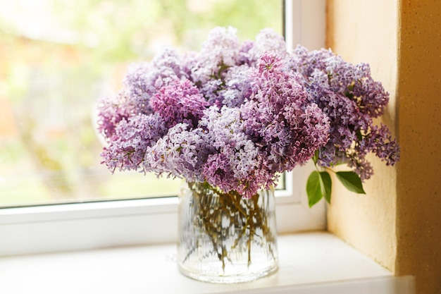 Belles fleurs lilas sur le rebord de la fenêtre dans une pièce ensoleillée Décor de chalet d'été avec des fleurs Lilas roses et violets dans un vase dans une maison rustique