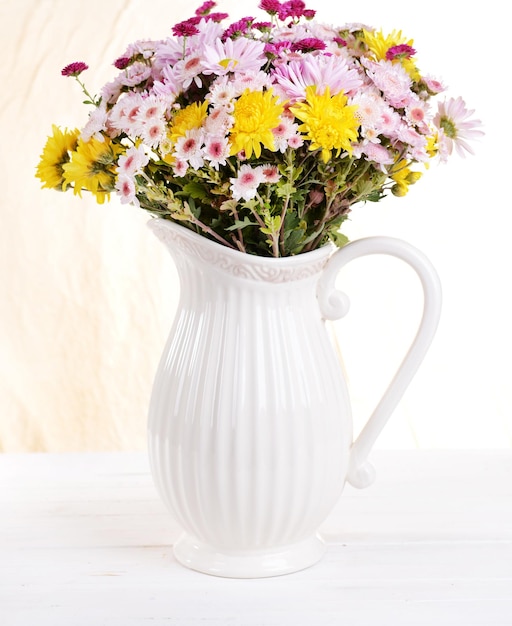 Belles fleurs en pichet sur table sur fond clair