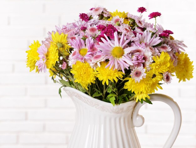 Belles fleurs en pichet sur table sur fond clair