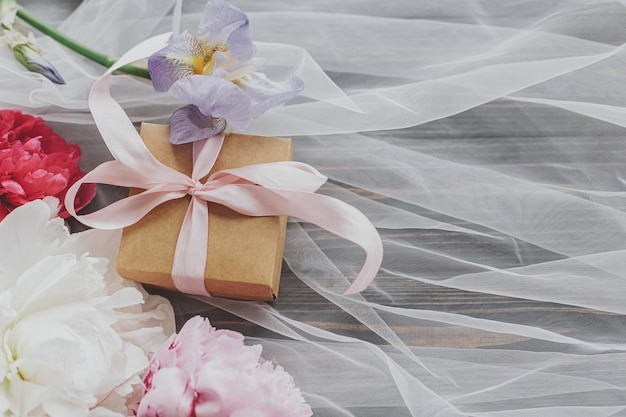 Photo belles fleurs de pivoine et d'iris et cadeau sur tissu doux sur la vue de dessus en bois foncé avec espace de copie