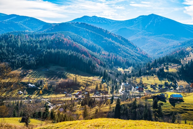 Belles forêts colorées couvrant les montagnes des Carpates et un petit village dans le contexte d'un ciel d'automne chaud