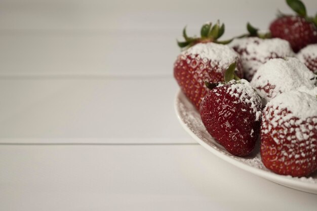 De belles fraises rouges juteuses et mûres saupoudrées de sucre en poudre sur une assiette ronde blanche