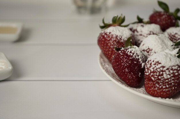 Photo de belles fraises rouges juteuses et mûres saupoudrées de sucre en poudre sur une assiette ronde blanche