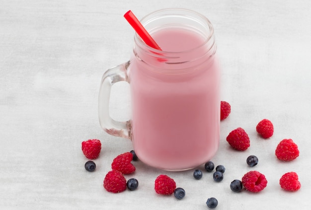 Belles framboises roses d'apéritif et smoothie de fruit de myrtille ou milkshake dans le pot en verre avec le fond de baies. Cocktail au yaourt. Fermer.