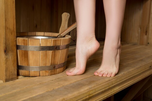 Belles jambes féminines dans le sauna, accessoires de bain. Seau en bois