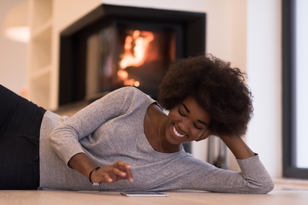 belles jeunes femmes noires utilisant une tablette sur le sol de sa maison de luxe devant la cheminée le jour de l'automne