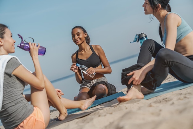 Belles jeunes femmes en vêtements de sport discutant de quelque chose avec le sourire et l'eau potable