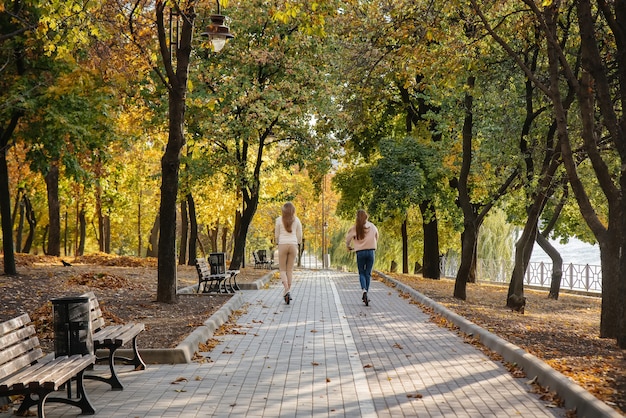 De belles jeunes filles montent dans le parc sur un scooter électrique par une chaude journée d'automne. Promenade dans le parc.