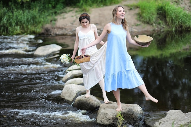 De belles jeunes filles en robes traversent le ruisseau le long des rochers