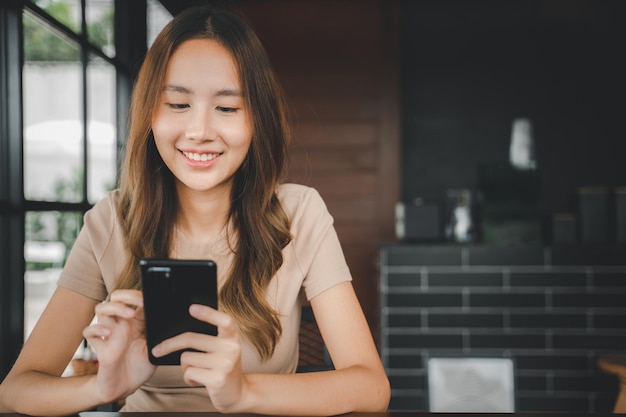 Belles mains féminines asiatiques tenant et tapant pour communiquer avec les autres via un téléphone portable, jeune femme utilisant un smartphone pour faire des achats en ligne au café-café près des fenêtres le matin