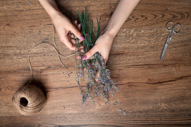 De belles mains féminines attachent un bouquet de lavande sèche sur le fond de la vue de dessus de table en chêne